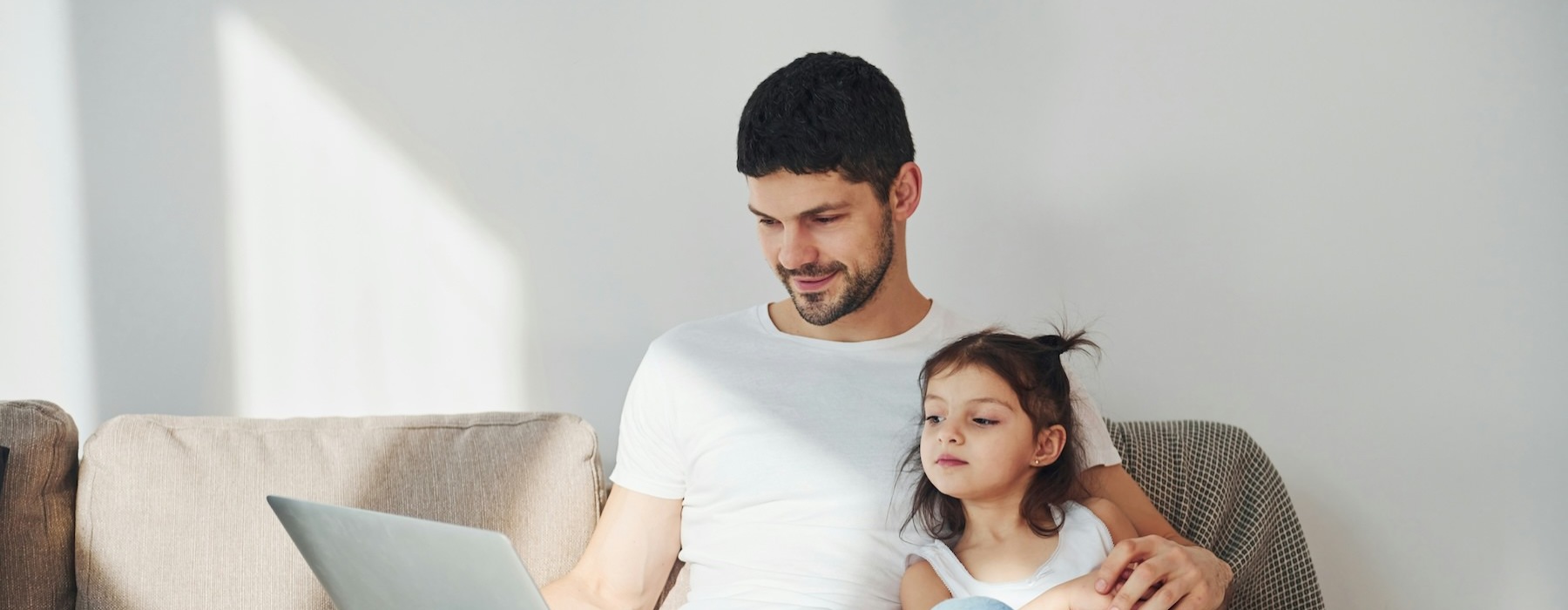 a person and a girl sitting on a couch looking at a laptop